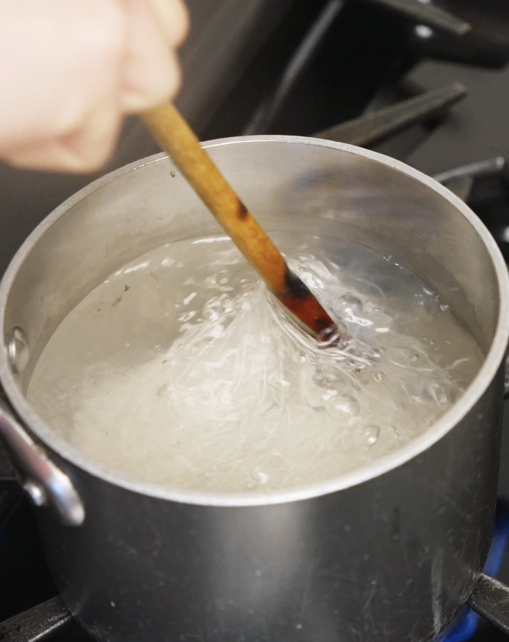 Vermicelli rice noodles being stirred in a pot of boiling water until tender for lemongrass chicken noodle bowls.