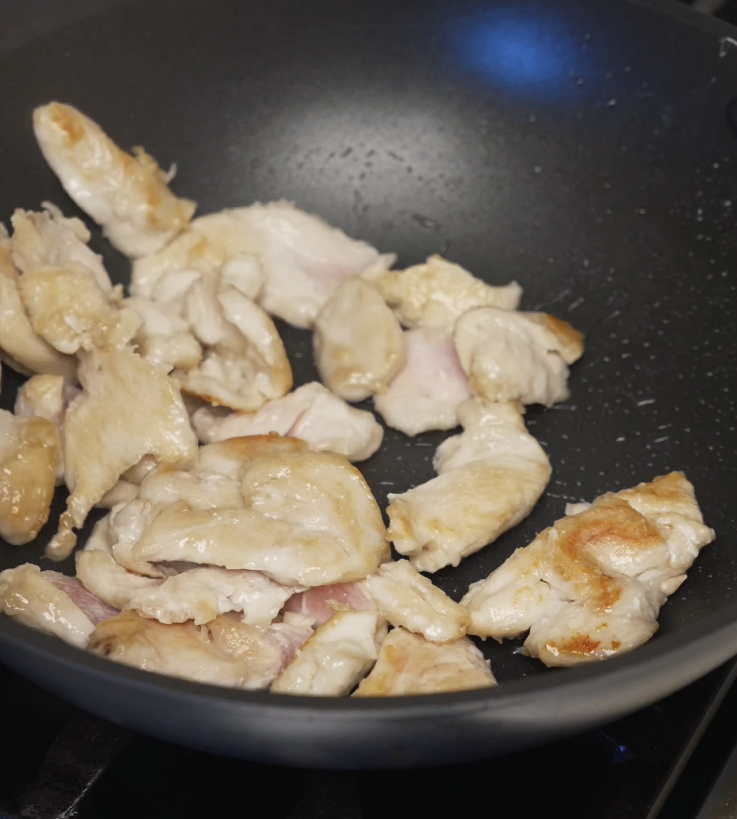 Thinly sliced chicken breast cooking in a hot pan until lightly browned and about 80 percent cooked through before being removed.
