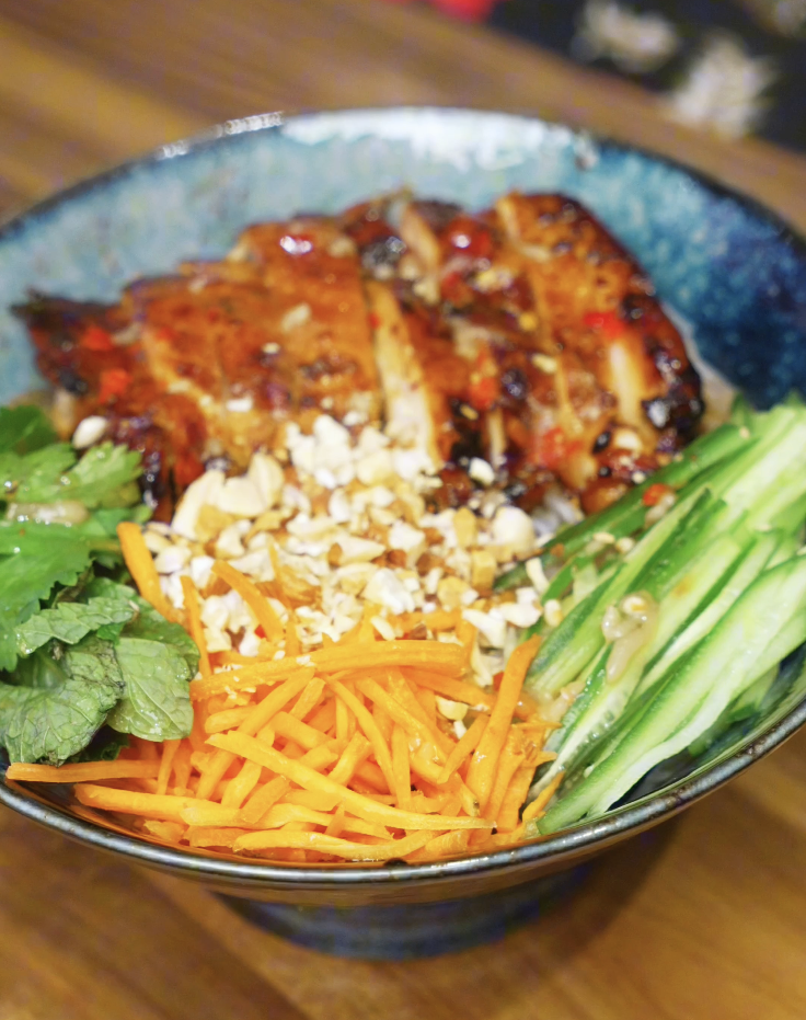 Vermicelli noodles topped with sliced lemongrass chicken, cucumber, shredded carrots, mint, and cilantro in a ceramic bowl.