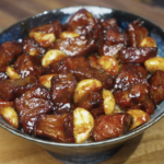 Bowl of garlic steak stir fry featuring glossy steak cubes and whole caramelized garlic cloves served over white rice.