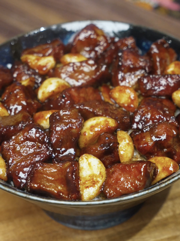 Bowl of garlic steak stir fry featuring glossy steak cubes and whole caramelized garlic cloves served over white rice.