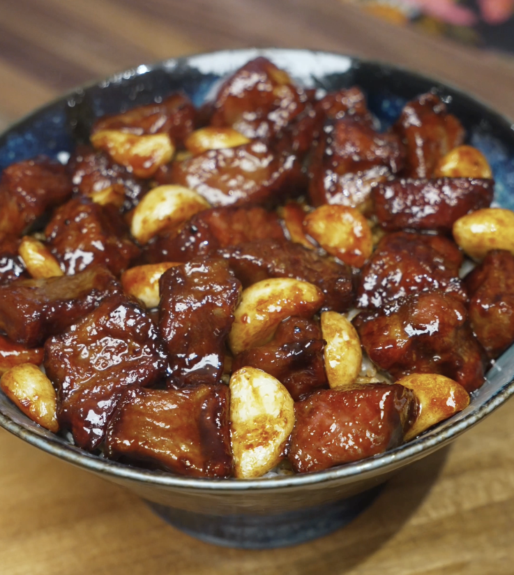 Bowl of garlic steak stir fry featuring glossy steak cubes and whole caramelized garlic cloves served over white rice.