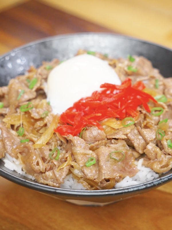 Finished gyudon bowl with thinly sliced beef and onions simmered in a sweet soy broth, topped with pickled ginger, scallions, and an onsen egg over rice.