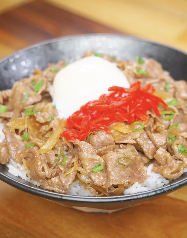Finished gyudon bowl with thinly sliced beef and onions simmered in a sweet soy broth, topped with pickled ginger, scallions, and an onsen egg over rice.