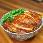 Soy sauce chicken sliced and served over steamed white rice with glossy sauce and leafy greens in a patterned bowl.