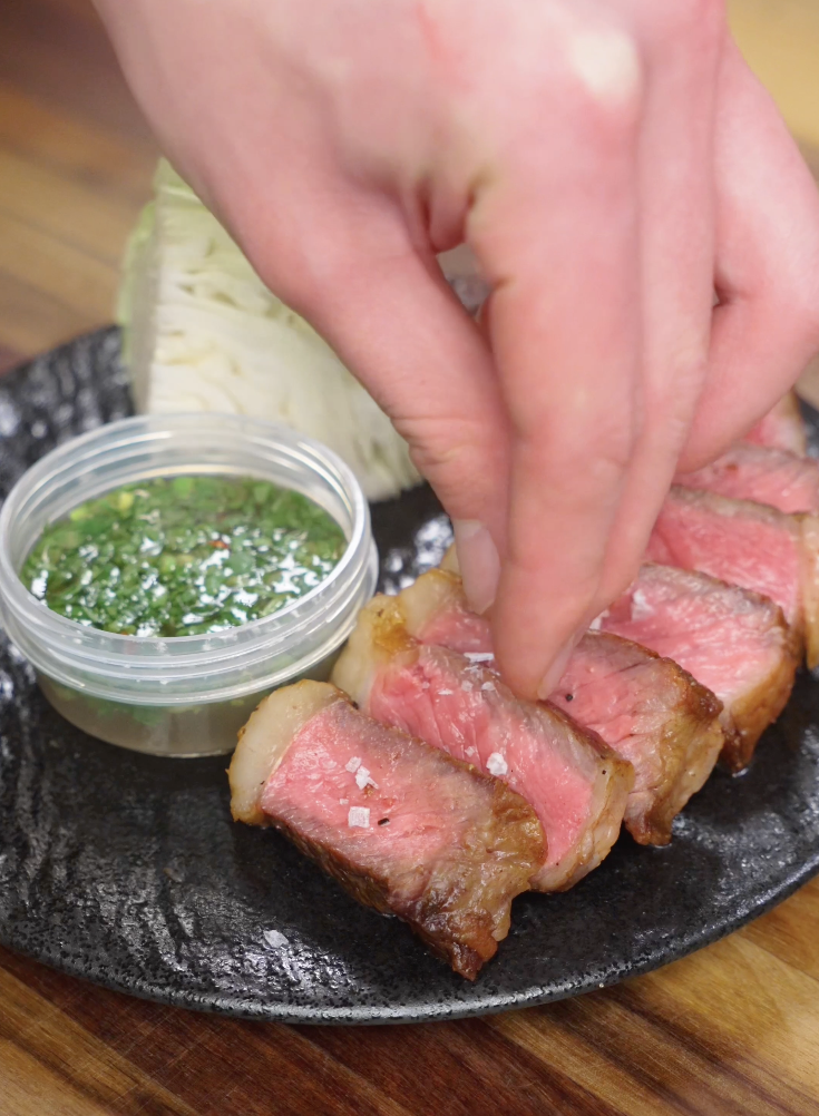 Flaky salt being sprinkled over sliced Crying Tiger Steak just before serving to enhance flavor and texture.