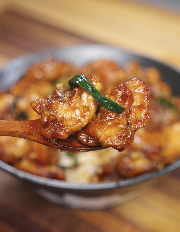 Close-up bite of garlic chicken stir fry on a wooden spoon, showing caramelized chicken pieces coated in a rich soy garlic sauce with scallions.