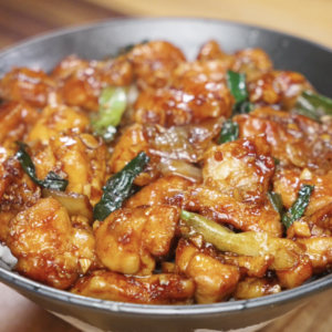 Finished bowl of garlic chicken stir fry with juicy chicken thigh pieces, onions, and scallions coated in a glossy savory garlic sauce, served as a healthy Asian dinner over rice.