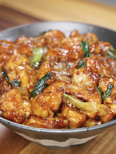 Finished bowl of garlic chicken stir fry with juicy chicken thigh pieces, onions, and scallions coated in a glossy savory garlic sauce, served as a healthy Asian dinner over rice.