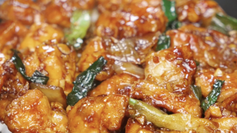 Finished bowl of garlic chicken stir fry with juicy chicken thigh pieces, onions, and scallions coated in a glossy savory garlic sauce, served as a healthy Asian dinner over rice.
