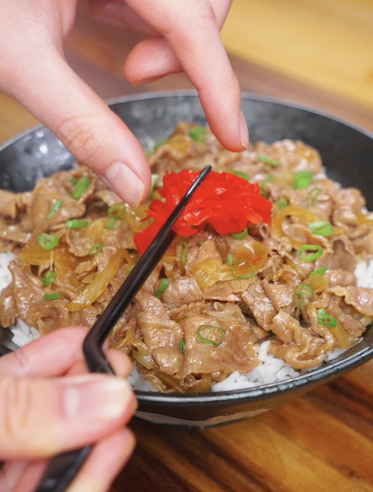 Adding bright red pickled ginger on top of a finished gyudon bowl to balance the rich, savory beef and onions.