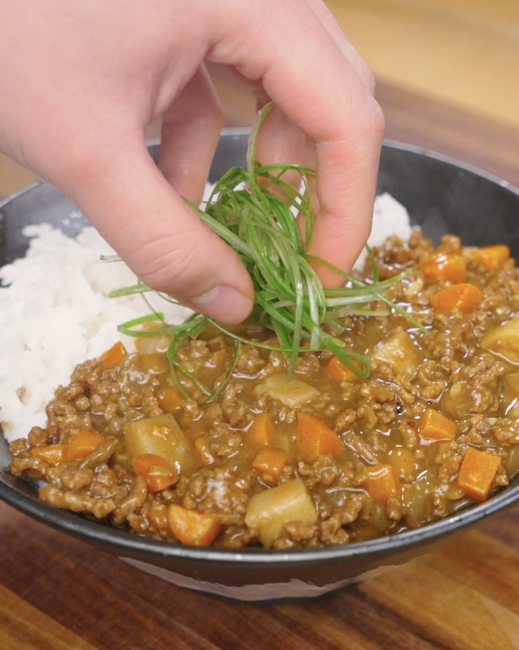 Freshly sliced scallions being added on top of Japanese ground beef curry served with rice for a final garnish.