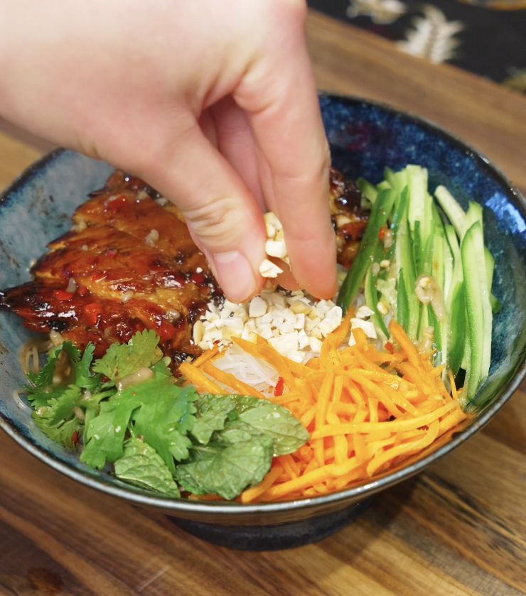 Hand sprinkling chopped peanuts over a lemongrass chicken noodle bowl for added crunch and texture.