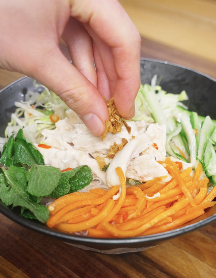 Crispy fried onions being sprinkled over shredded chicken and vegetables to finish Vietnamese chicken salad.