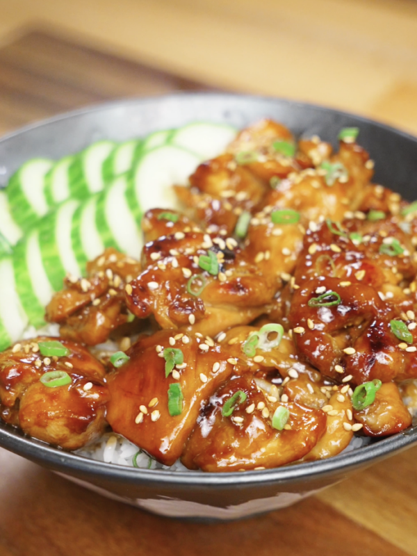 Finished bowl of honey garlic chicken served over white rice with sliced cucumbers, sesame seeds, and scallions, showcasing a glossy caramelized honey garlic glaze as a healthy Asian dinner.