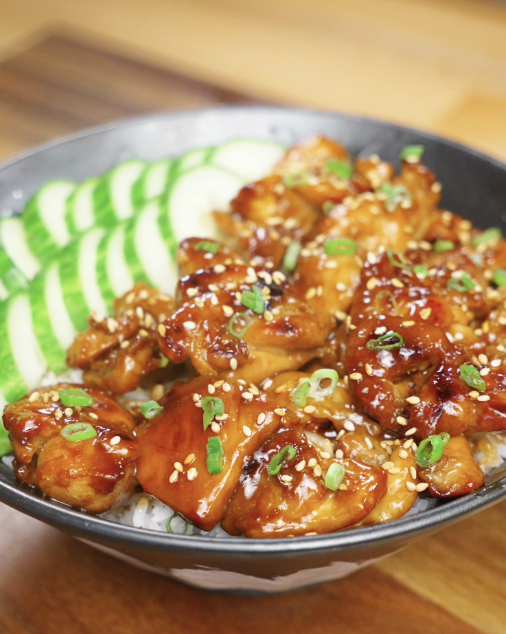 Finished bowl of honey garlic chicken served over white rice with sliced cucumbers, sesame seeds, and scallions, showcasing a glossy caramelized honey garlic glaze as a healthy Asian dinner.