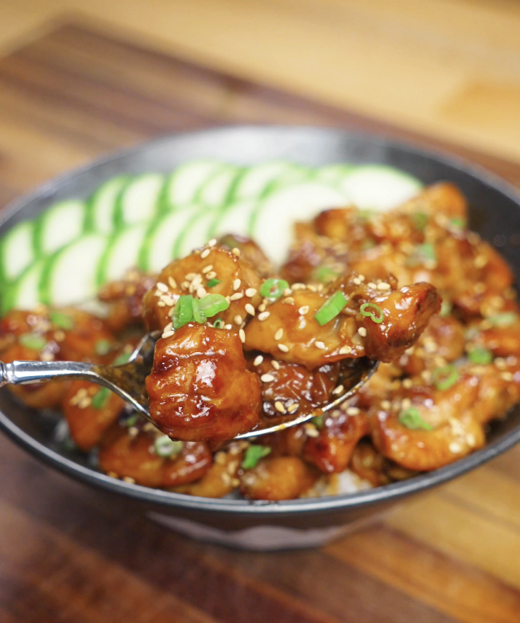 Close-up spoonful of honey garlic chicken featuring juicy bite-sized chicken thighs coated in a glossy sweet and savory honey soy garlic glaze, garnished with sesame seeds and scallions over steamed rice.