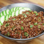 Finished bowl of Korean BBQ beef made with savory, slightly sweet ground beef cooked in a glossy soy-sesame sauce, served over steamed rice with sliced cucumbers, scallions, and sesame seeds as a healthy Asian dinner.