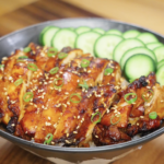 Finished bowl of Korean BBQ chicken served over rice with caramelized sliced chicken thighs, fresh cucumbers, sesame seeds, and scallions as a healthy Asian dinner.