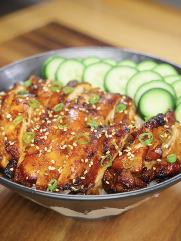 Finished bowl of Korean BBQ chicken served over rice with caramelized sliced chicken thighs, fresh cucumbers, sesame seeds, and scallions as a healthy Asian dinner.