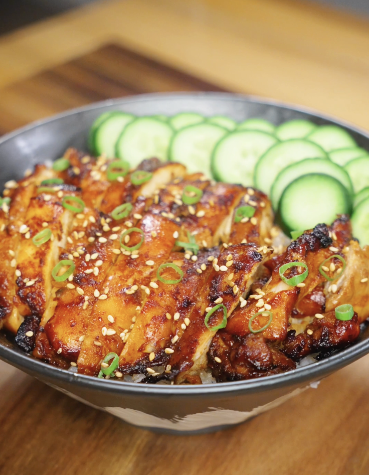 Finished bowl of Korean BBQ chicken served over rice with caramelized sliced chicken thighs, fresh cucumbers, sesame seeds, and scallions as a healthy Asian dinner.