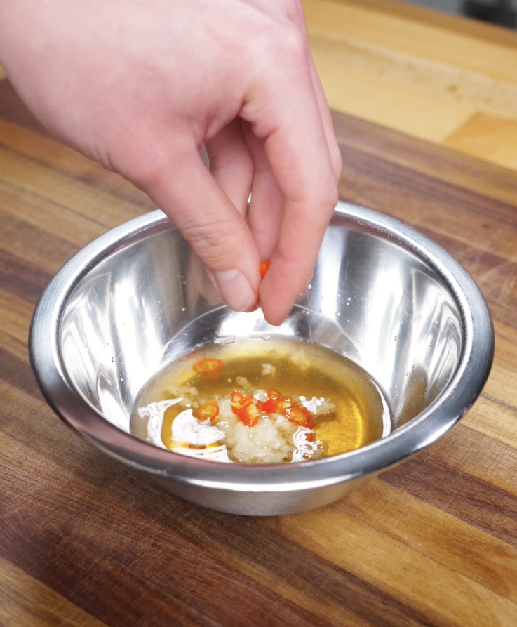 Fish sauce dressing being mixed in a metal bowl with lime juice, vinegar, minced garlic, sliced Thai chilies, and sugar for Vietnamese chicken salad.