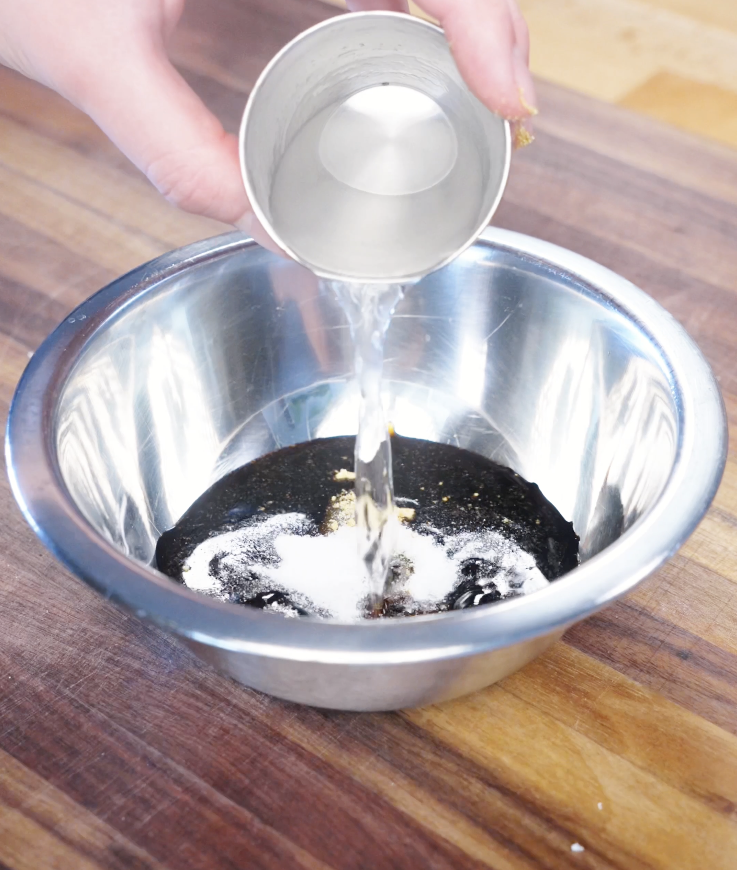 Pouring water into a bowl with soy sauce, oyster sauce, sugar, and chicken bouillon to create the savory garlic stir fry sauce.