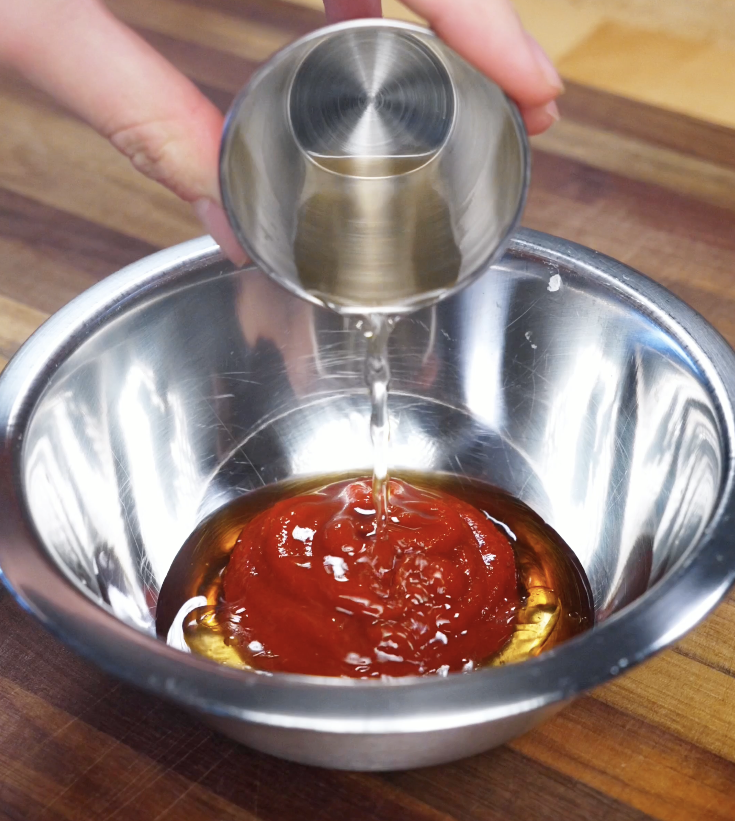 Gochujang sauce being mixed in a stainless steel bowl with sesame oil, rice vinegar, garlic, and sugar to create a bold bibimbap sauce.