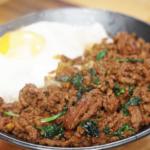 Finished bowl of Pad Kra Pao made with savory, spicy ground beef cooked in a soy and fish sauce glaze, served over steamed white rice with a crispy fried egg and fresh basil as a healthy Asian dinner.