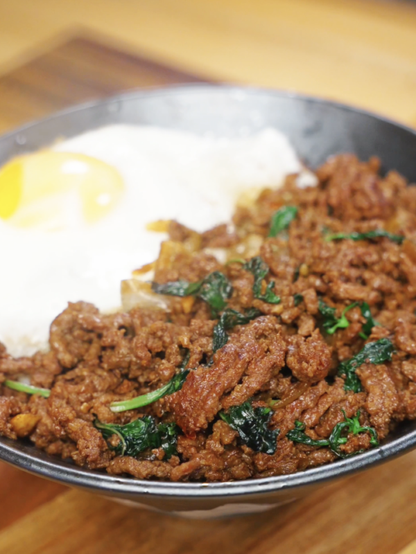 Finished bowl of Pad Kra Pao made with savory, spicy ground beef cooked in a soy and fish sauce glaze, served over steamed white rice with a crispy fried egg and fresh basil as a healthy Asian dinner.