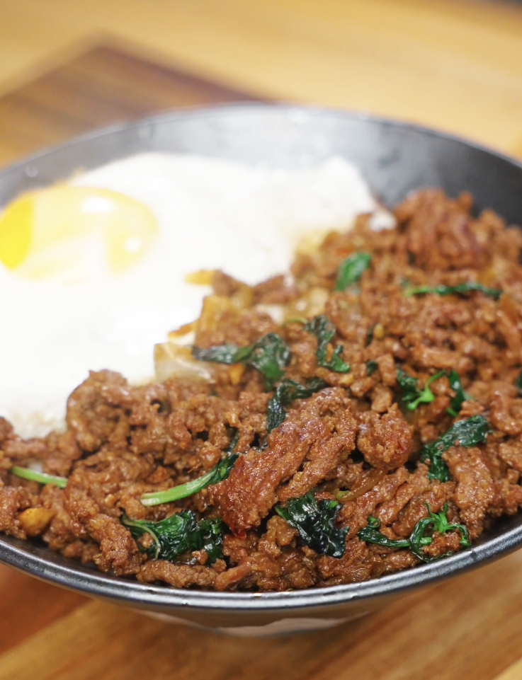 Finished bowl of Pad Kra Pao made with savory, spicy ground beef cooked in a soy and fish sauce glaze, served over steamed white rice with a crispy fried egg and fresh basil as a healthy Asian dinner.