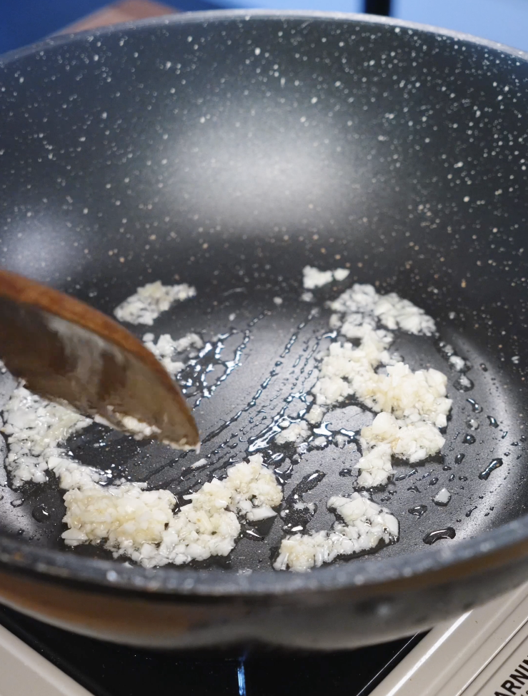 Minced garlic and ginger sizzling in neutral oil in a nonstick pan as the first cooking step for Korean BBQ beef.