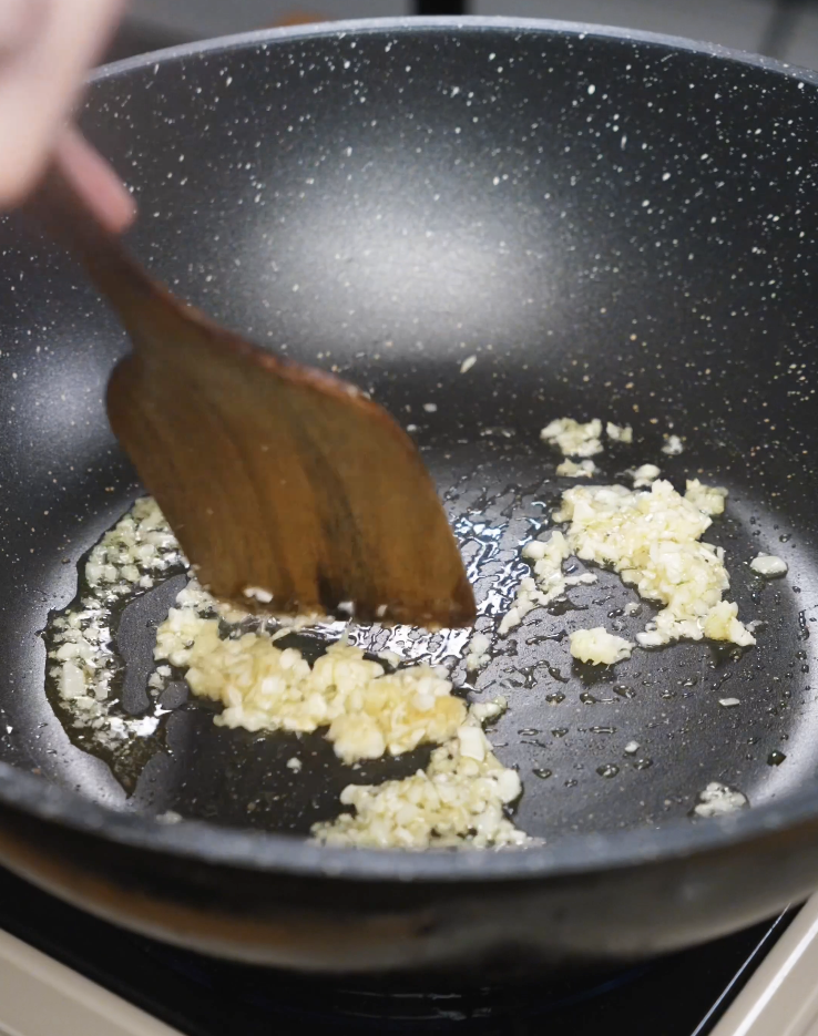 Minced garlic being saut&eacute;ed in oil in a nonstick pan until fragrant before adding ground chicken for Spicy Peanut Chicken.