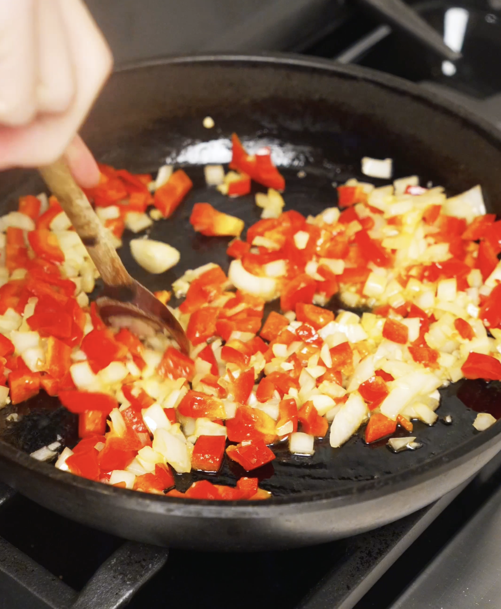 Diced red bell peppers and onions being saut&eacute;ed in oil until softened and fragrant in a skillet.