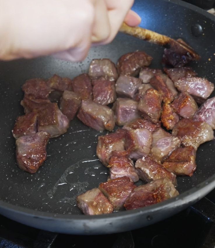 Cubed flatiron steak browning in a pan after caramelized garlic has been removed.