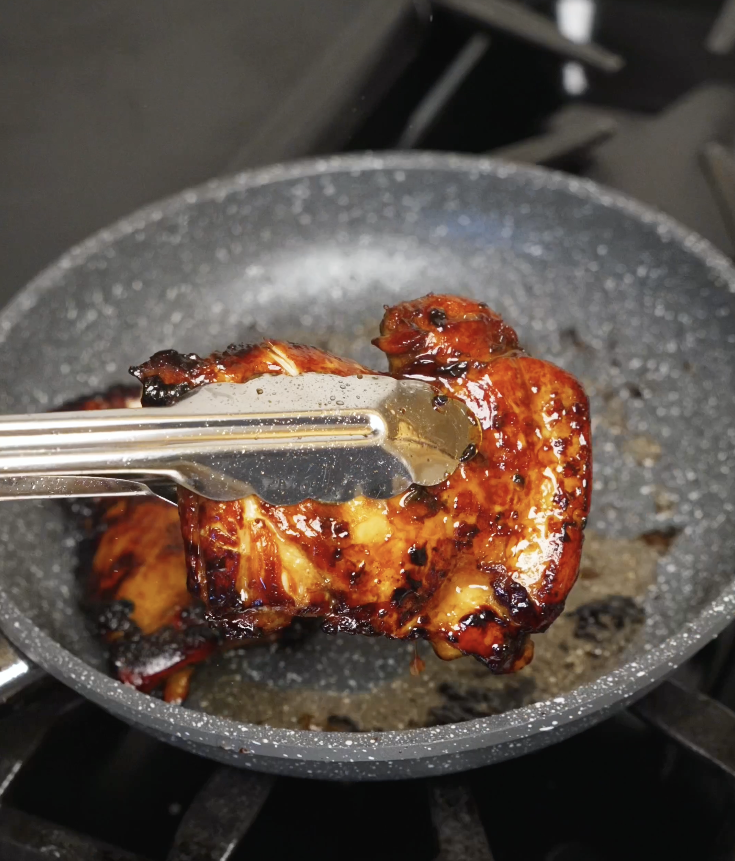 Marinated lemongrass chicken thighs searing in a hot nonstick pan until caramelized and golden brown.