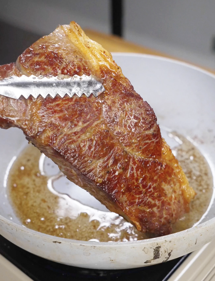 Steak being seared in a hot pan with oil, developing a deep golden crust as the first step in making Crying Tiger Steak.