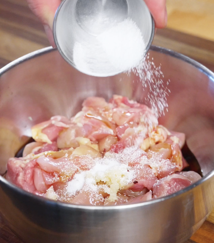 Raw cubed chicken thighs being seasoned with salt, garlic, and marinade ingredients in a stainless steel bowl as the first step of chicken bibimbap.