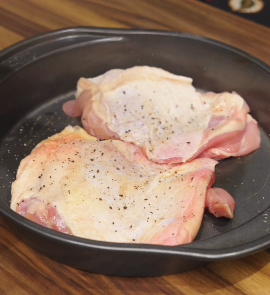 Raw skin-on chicken thighs seasoned with salt and black pepper on a baking tray before searing for teriyaki chicken.