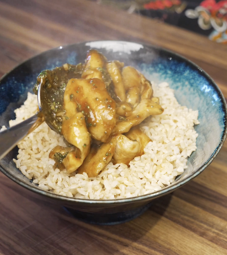 Saucy chicken and broccoli being spooned over a bowl of steamed rice, finishing the classic chicken and broccoli dish.