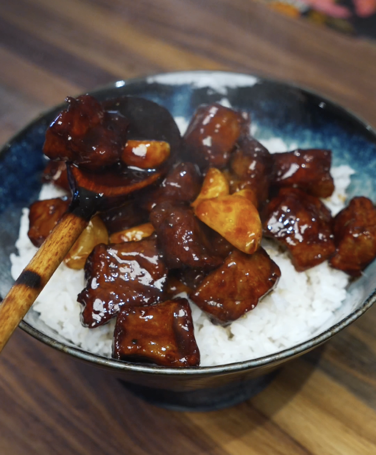 Garlic steak stir fry being spooned over a bowl of steamed white rice with glossy sauce and caramelized garlic.