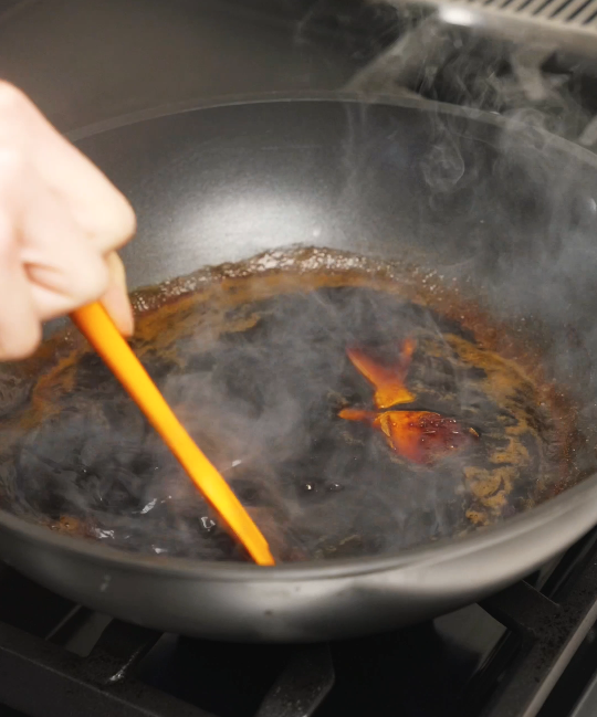 Soy sauce, sugar, ginger, and spices simmering in a pan with steam rising, forming the deeply savory braising base for soy sauce chicken.