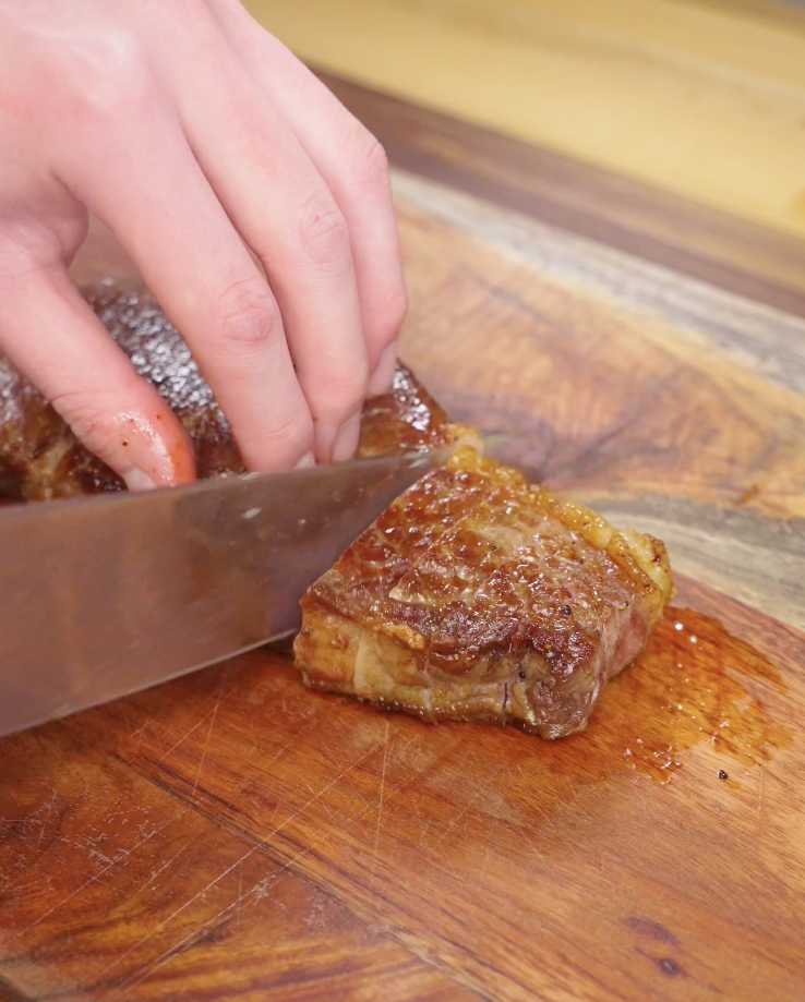 Cooked Crying Tiger Steak being sliced thinly against the grain on a wooden cutting board for optimal tenderness.