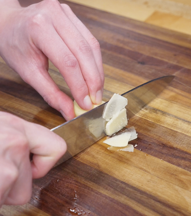 Thinly slicing onion, fresh ginger, and garlic on a cutting board to build the fragrant base for golden oil poached chicken.