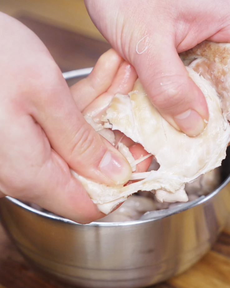 Juicy poached chicken thighs being sliced into tender pieces so they can soak up the soy-forward golden oil sauce before serving over rice.
