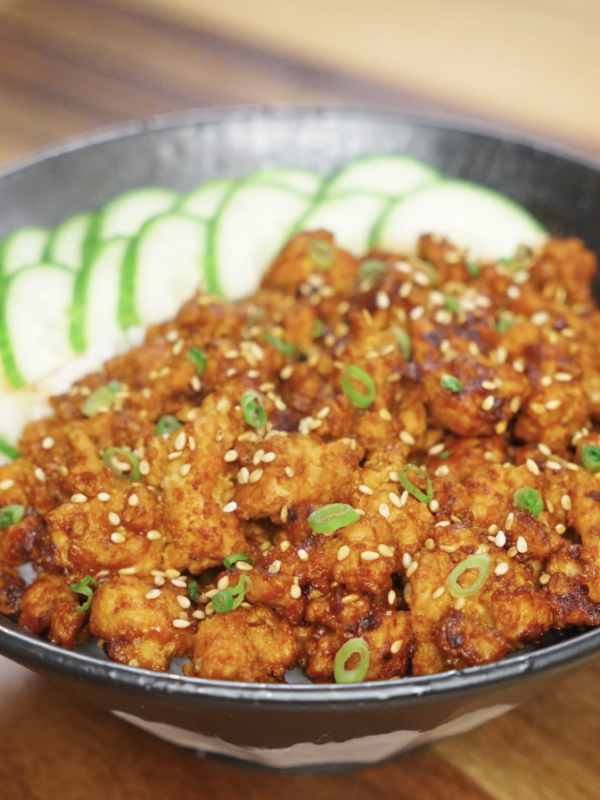 Finished bowl of Spicy Peanut Chicken made with ground chicken cooked in a creamy gochujang peanut sauce, served over steamed rice with sliced cucumbers, sesame seeds, and scallions as a healthy Asian dinner.