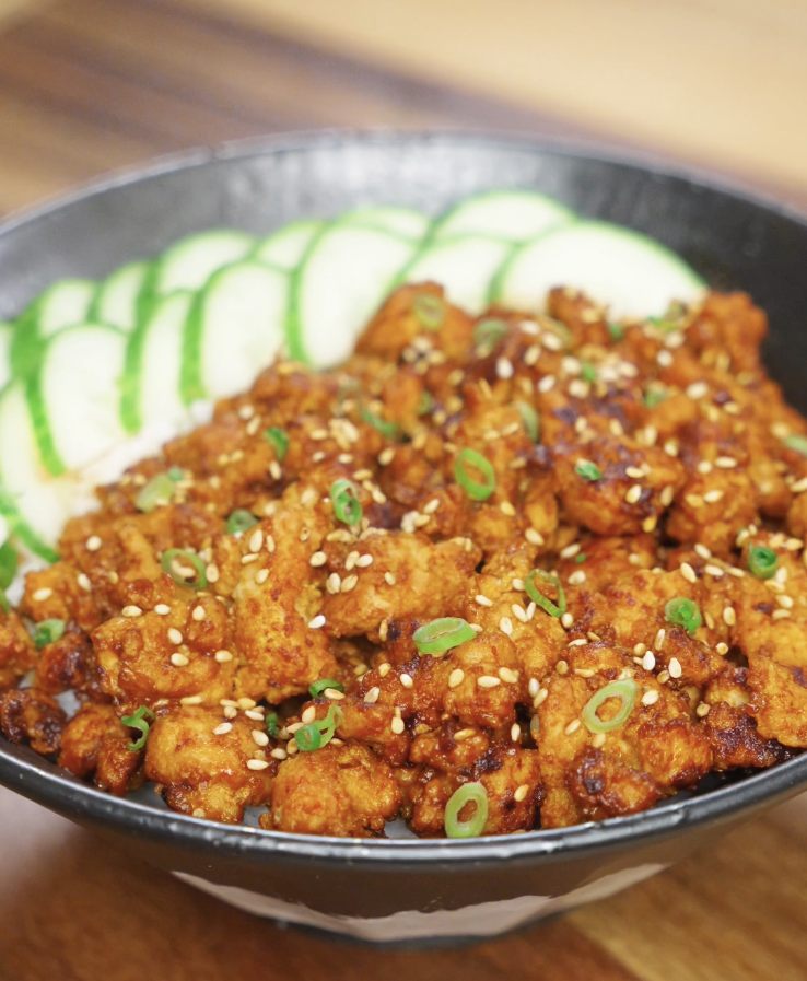 Finished bowl of Spicy Peanut Chicken made with ground chicken cooked in a creamy gochujang peanut sauce, served over steamed rice with sliced cucumbers, sesame seeds, and scallions as a healthy Asian dinner.