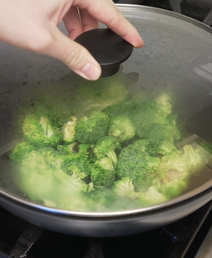 Broccoli florets steaming in a covered pan to soften while keeping their bright green color before being added back to the stir fry.