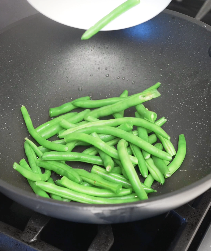 Fresh green string beans added to a hot pan and stir fried until bright green and slightly tender.