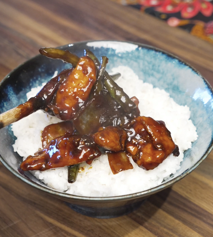 Spoonful of glossy string bean chicken served over steamed white rice, featuring tender chicken breast and crisp green beans coated in a savory soy-based stir fry sauce for a healthy Asian dinner.